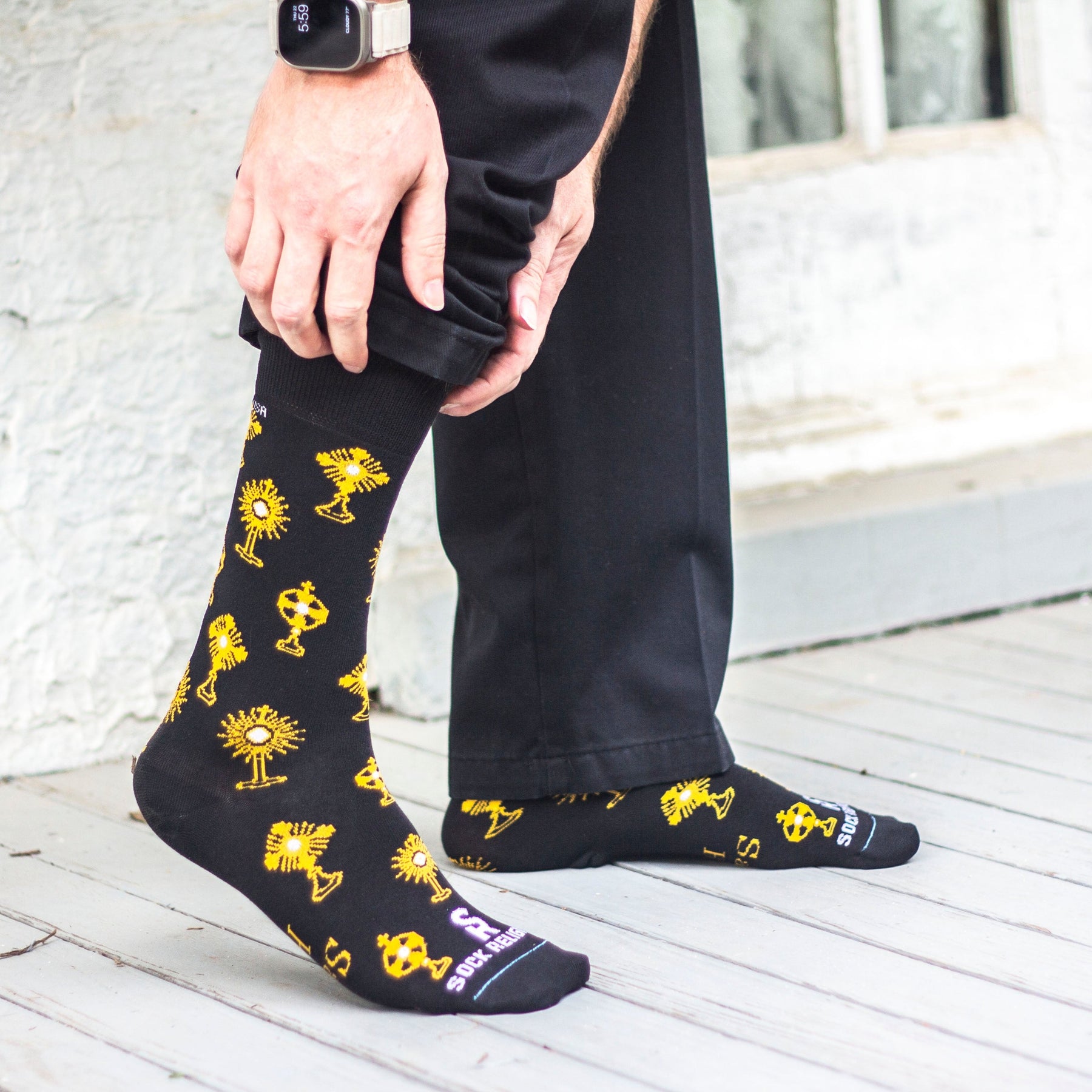 A person's foot in sleek black socks with shiny yellow designs kneeling down to adjust their pant leg