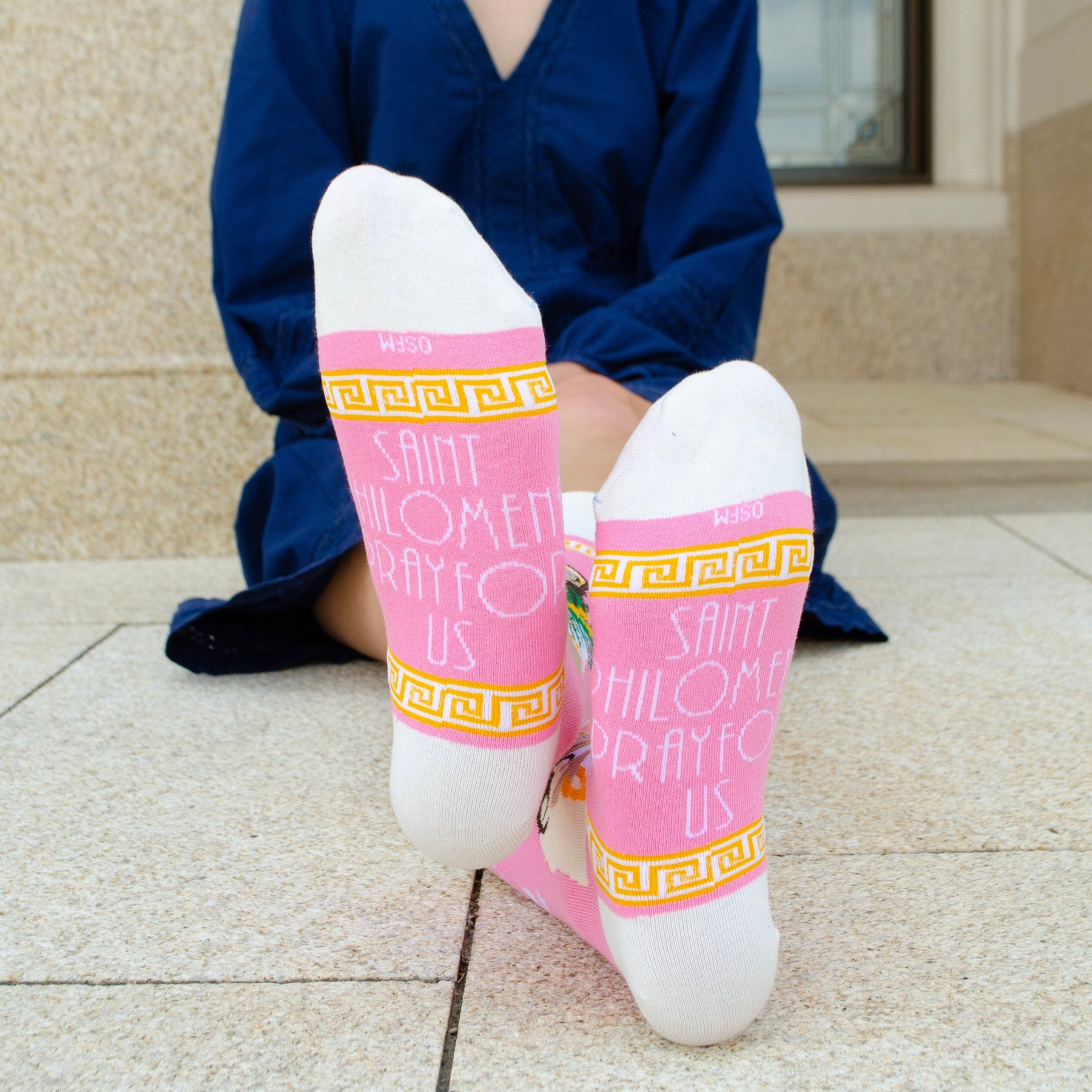A person sitting on the ground wearing a pair of pink and white socks with a picture of St. Philomena on it