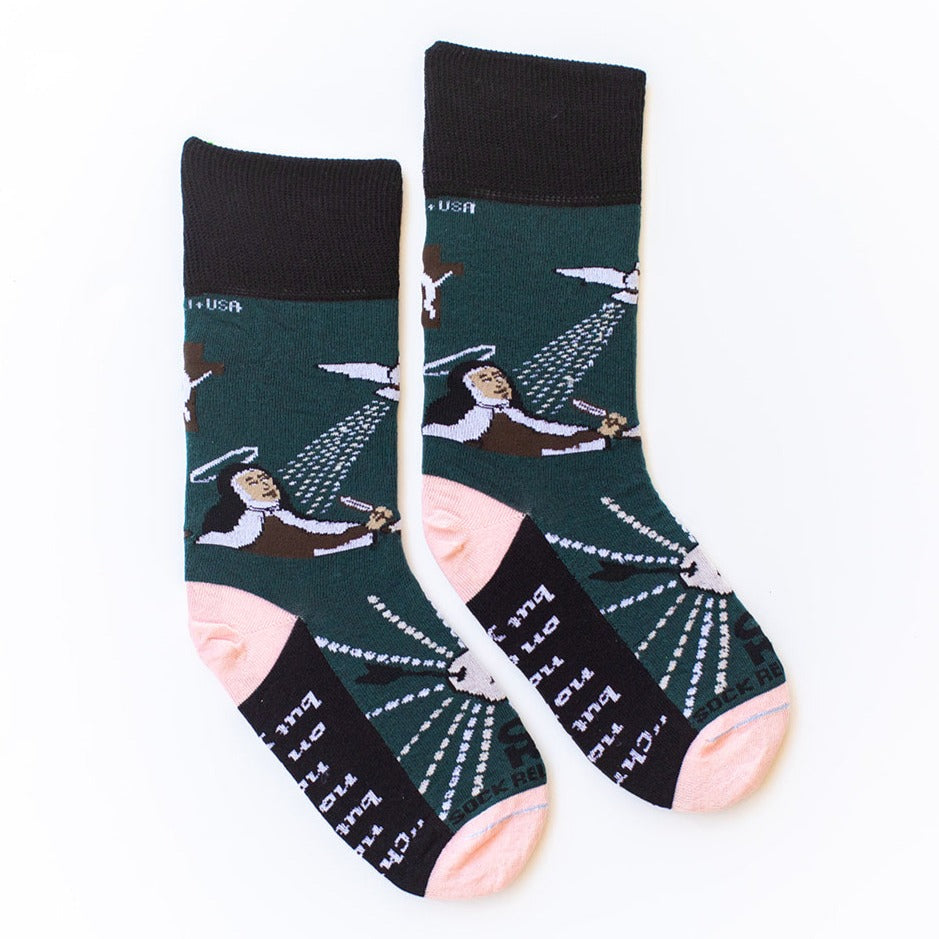 A pair of black, green, and pink St. Teresa of Ávila socks featuring a woman holding a quill and cross.