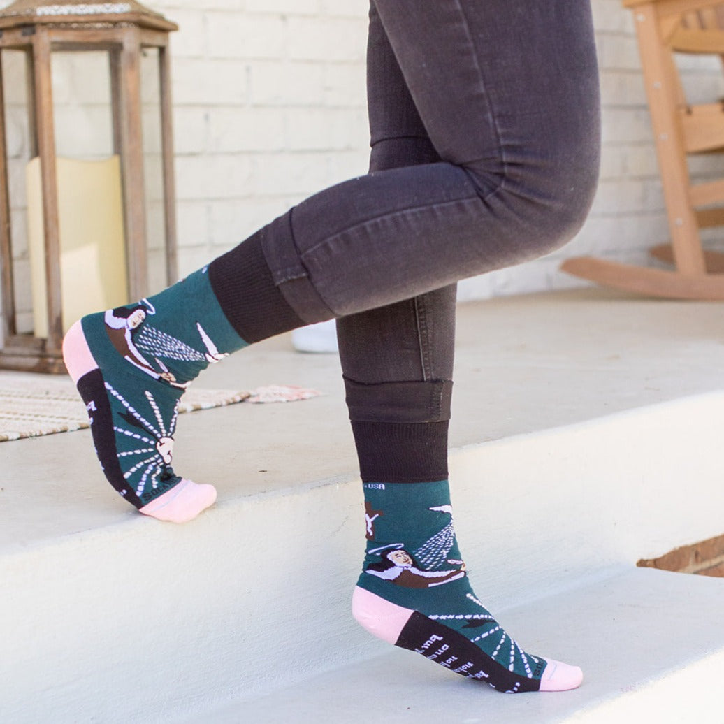 a woman standing on a step wearing a pair of black, green and pink St. Teresa of Avila socks