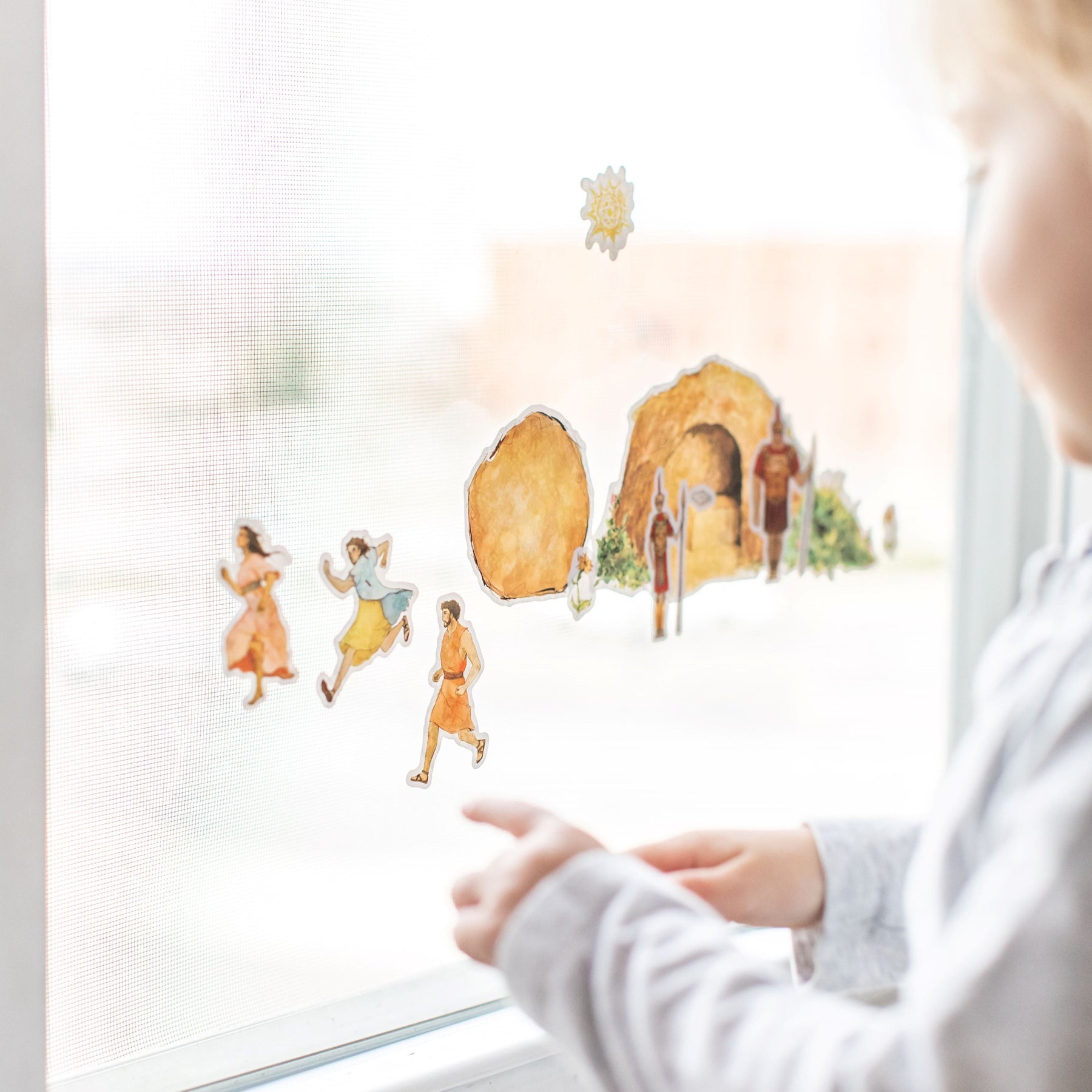 close up of little boy playing with empty tomb cling set on a window