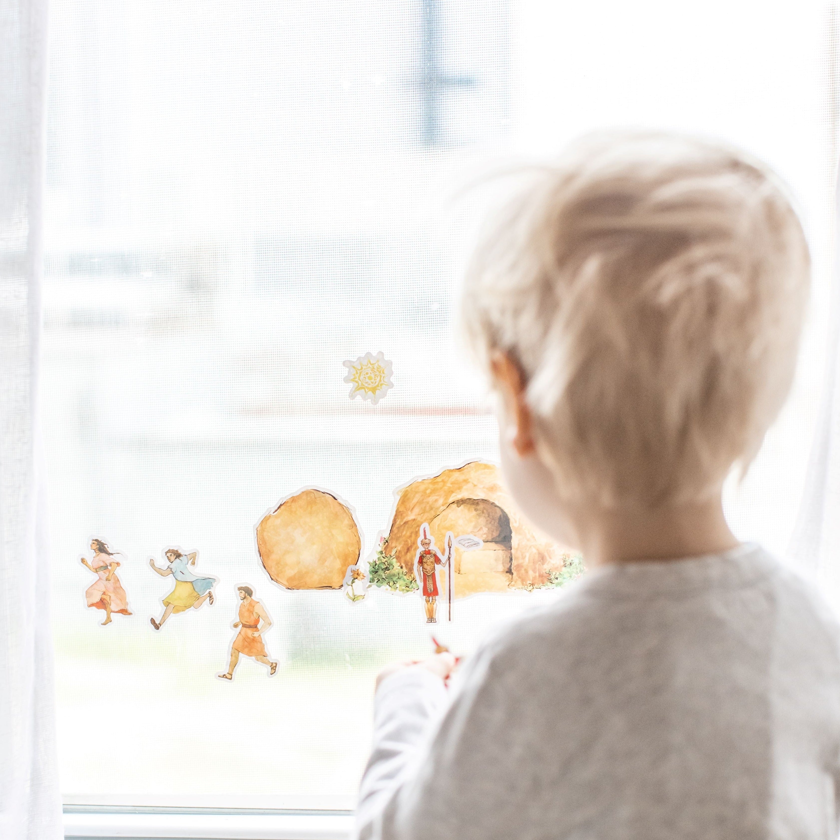 little boy playing with empty tomb cling set on a window, image from straight behind