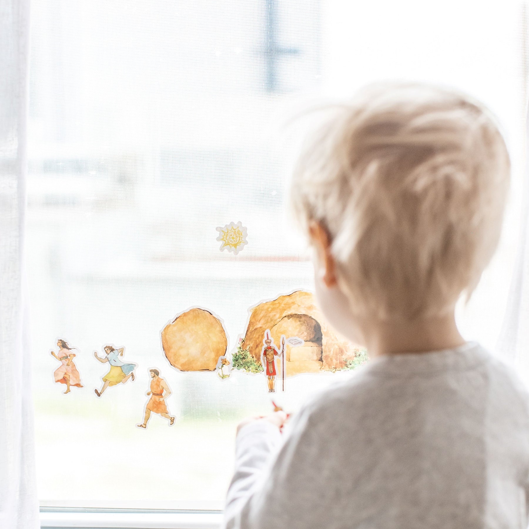 little boy playing with empty tomb cling set on a window, image from straight behind