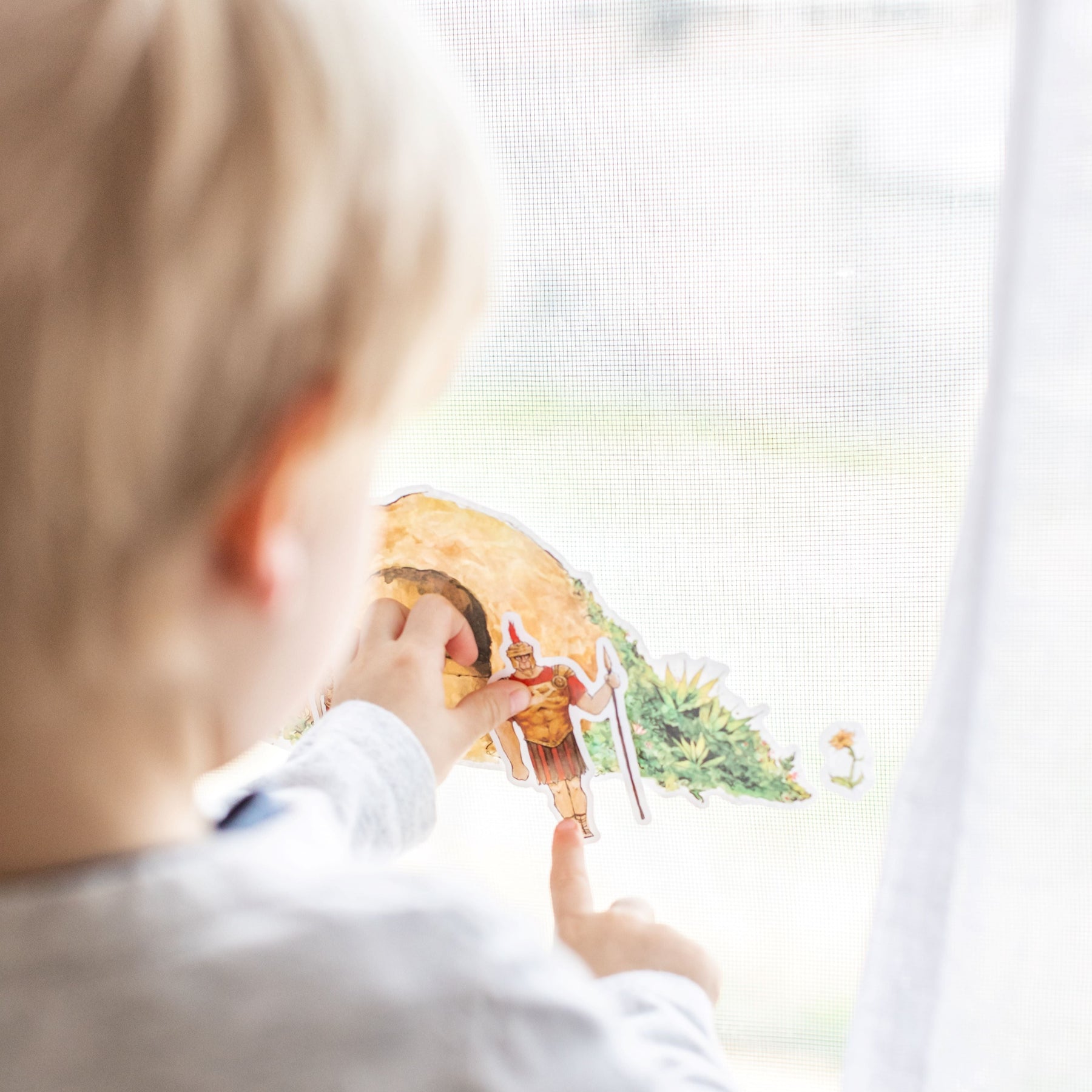 little boy playing with empty tomb cling set on a window, close up image from straight behind