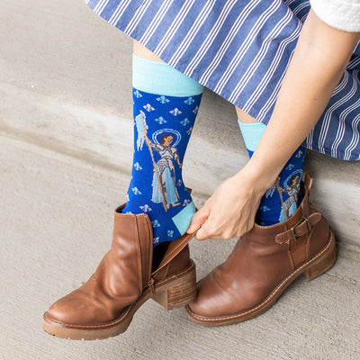 a woman wearing blue dress socks with St. Joan of Arc on them with a fleur de lis pattern on them with brown boots