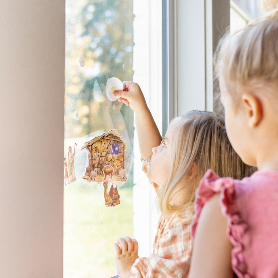 close up of little girls playing with Nativity Cling set on a window, little girl is putting up the star