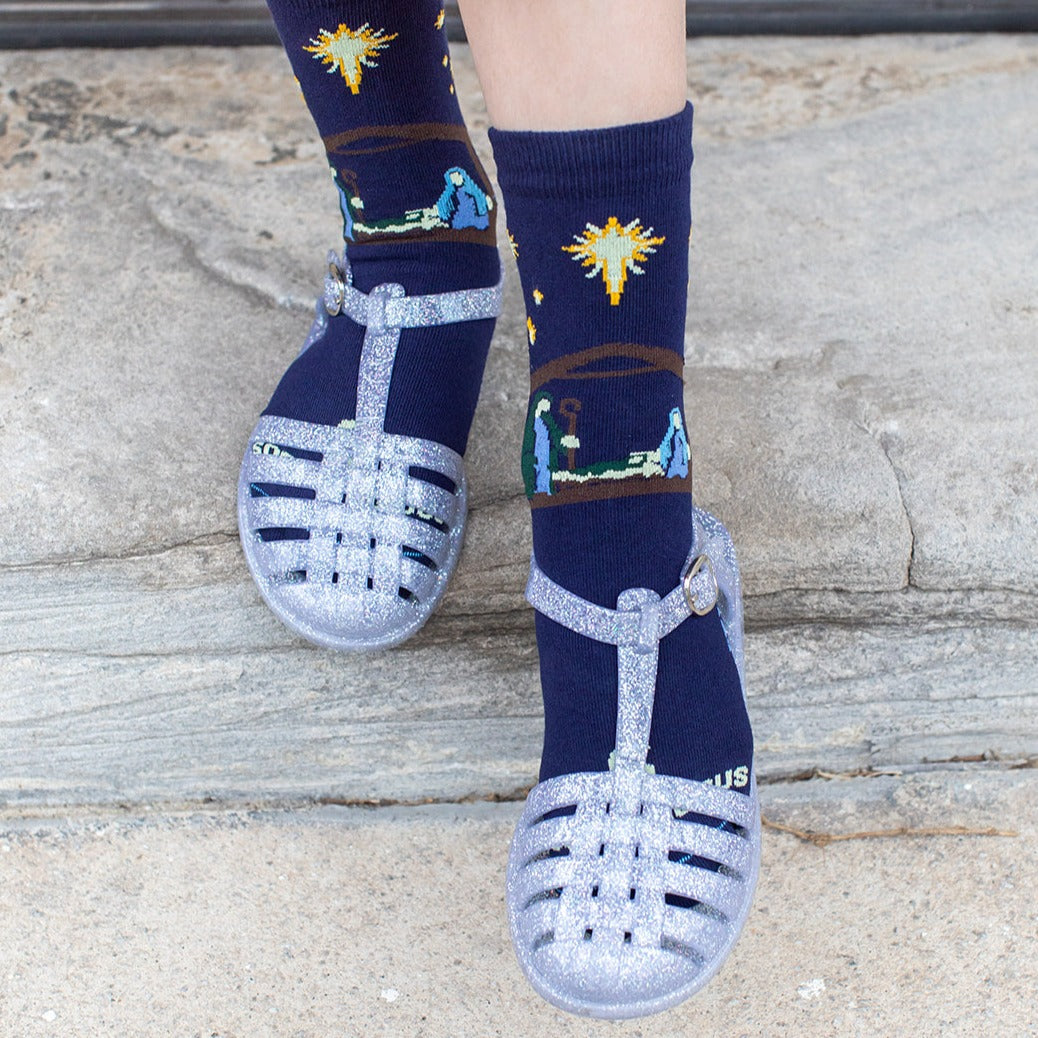 girl wearing shoes and dark navy blue socks featuring simple silhouettes of the manger scene