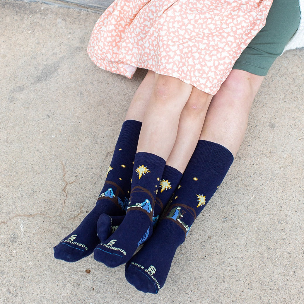 girl sitting in moms lap wearint dark navy blue socks featuring simple silhouettes of the manger scene
