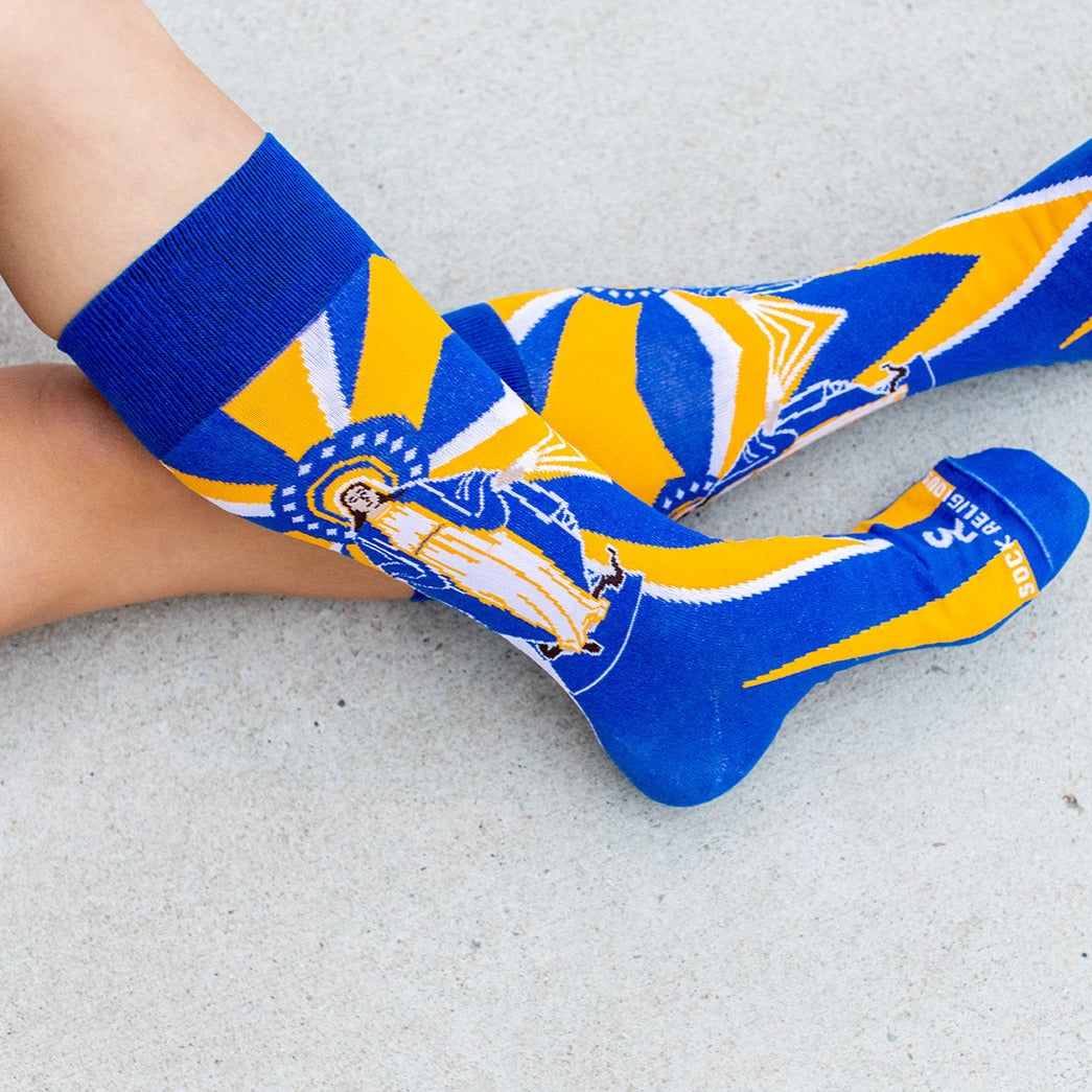 woman wearing Our Lady of Grace socks with Mary, yellow and blue rays and a serpant on the bottom of the foot
