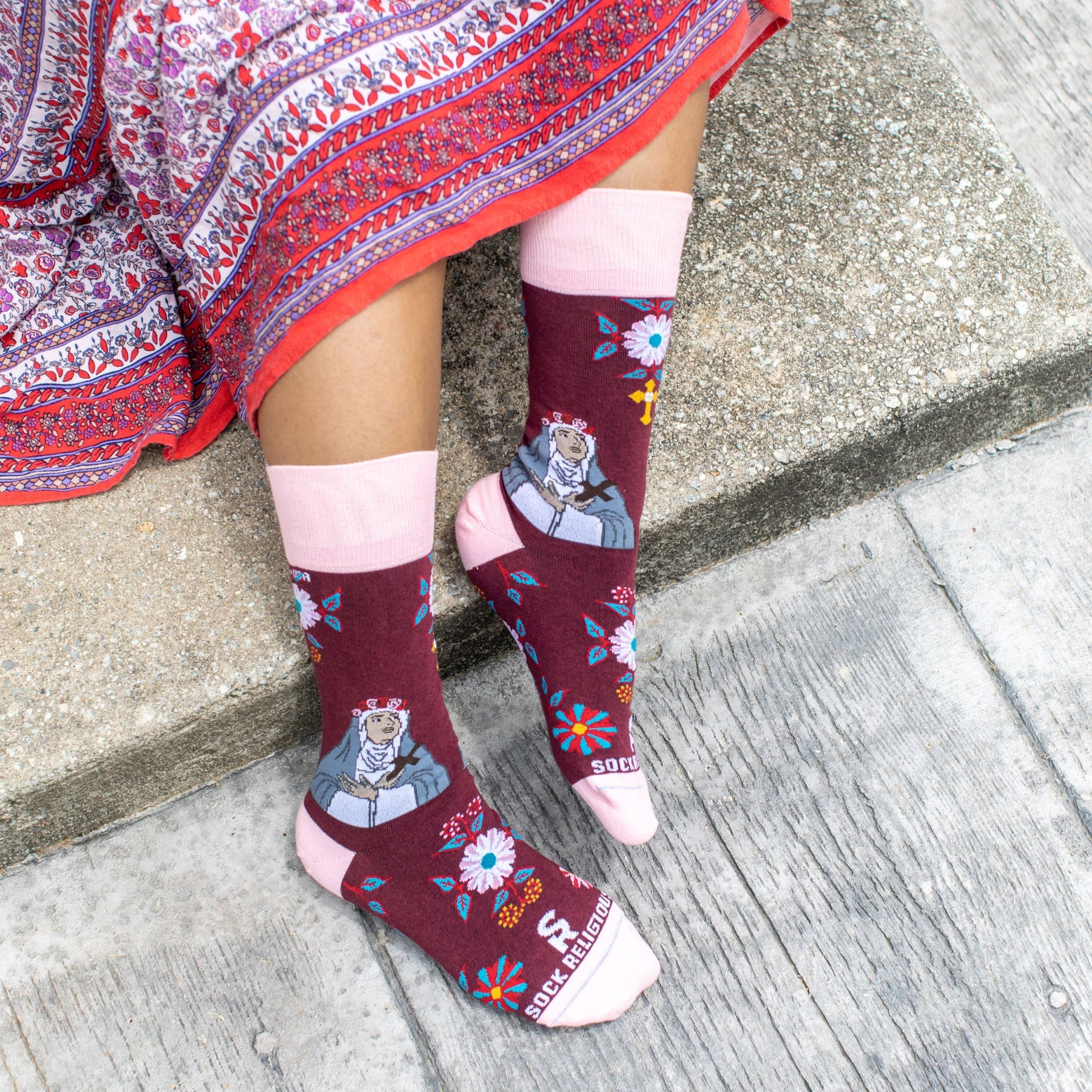 A person sitting and steps wearing a pair of pink and red sock with a picture of St. Rose of Lima on it