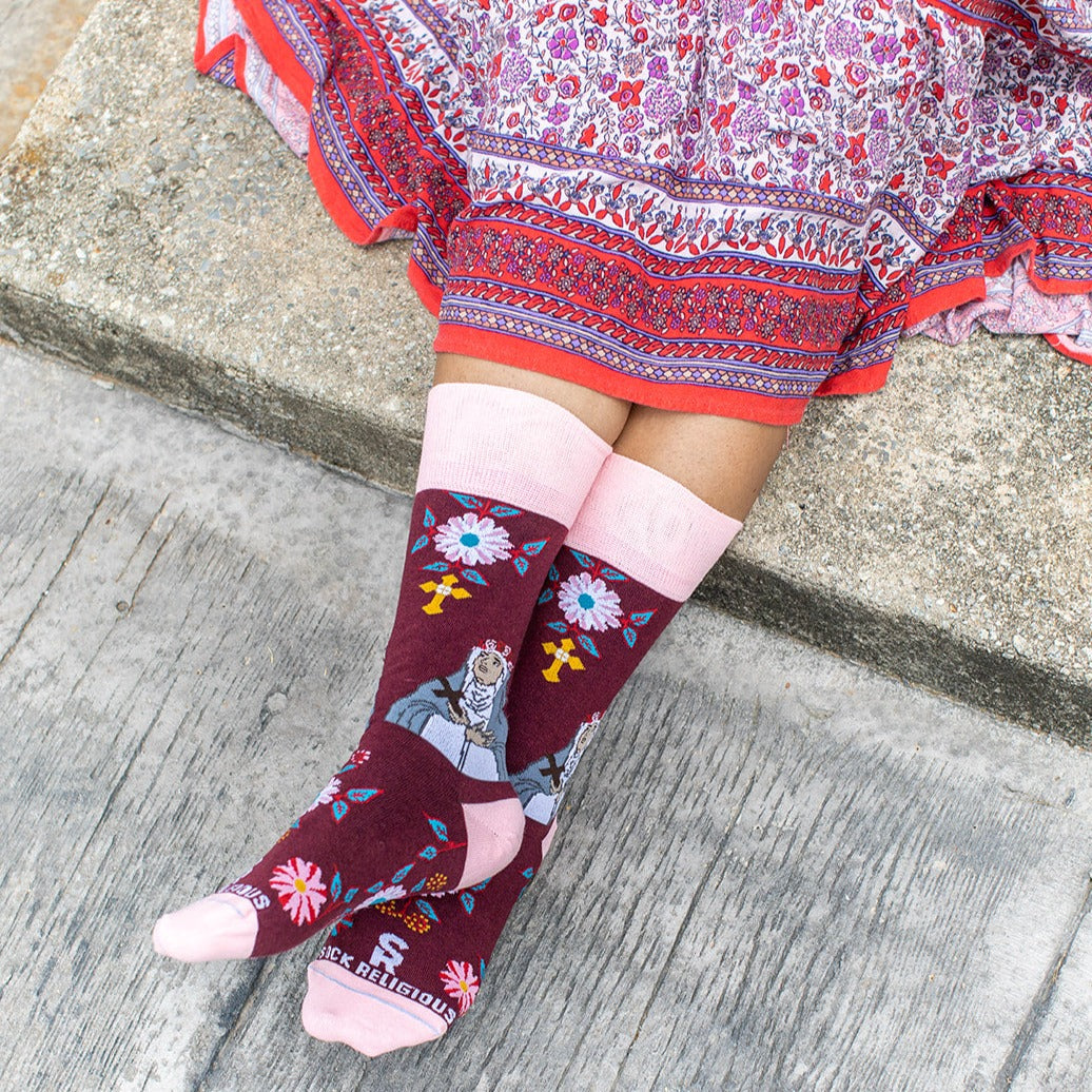 A person sitting on steps wearing a pair of pink and red sock with a picture of St. Rose of Lima on it