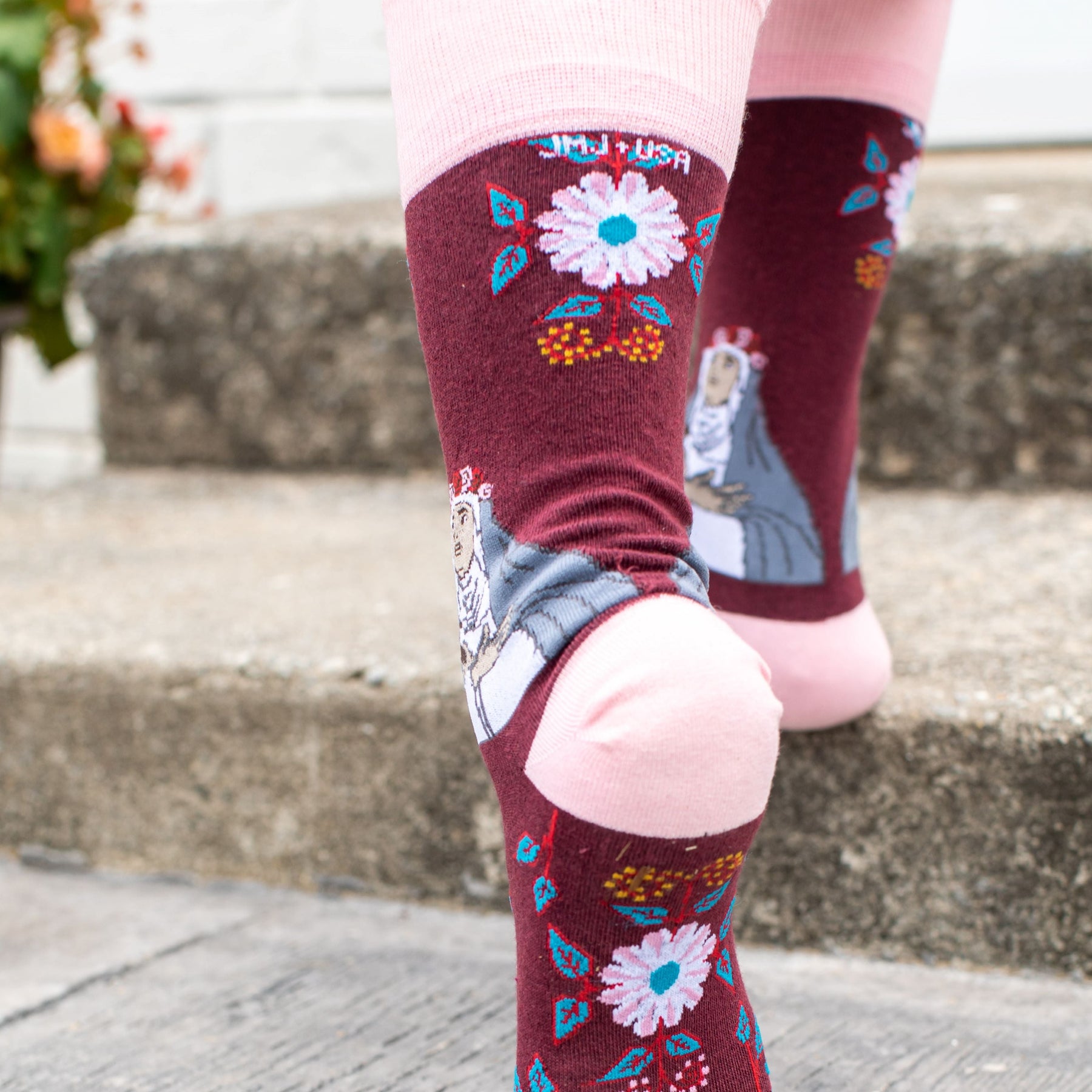 A person walking on steps wearing a pair of pink and red sock with a picture of St. Rose of Lima on it