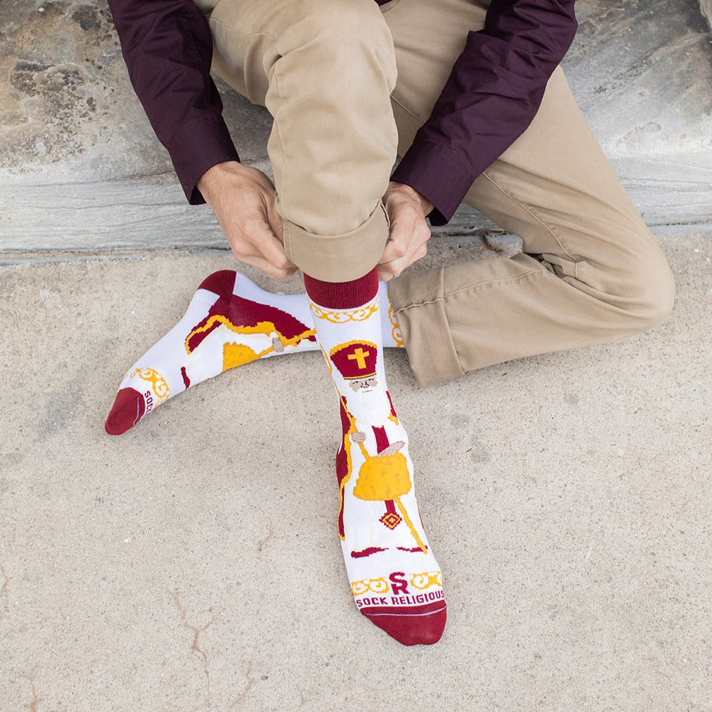 a man sitting on the ground wearing a pair of socks with an picture of St. Nicholas