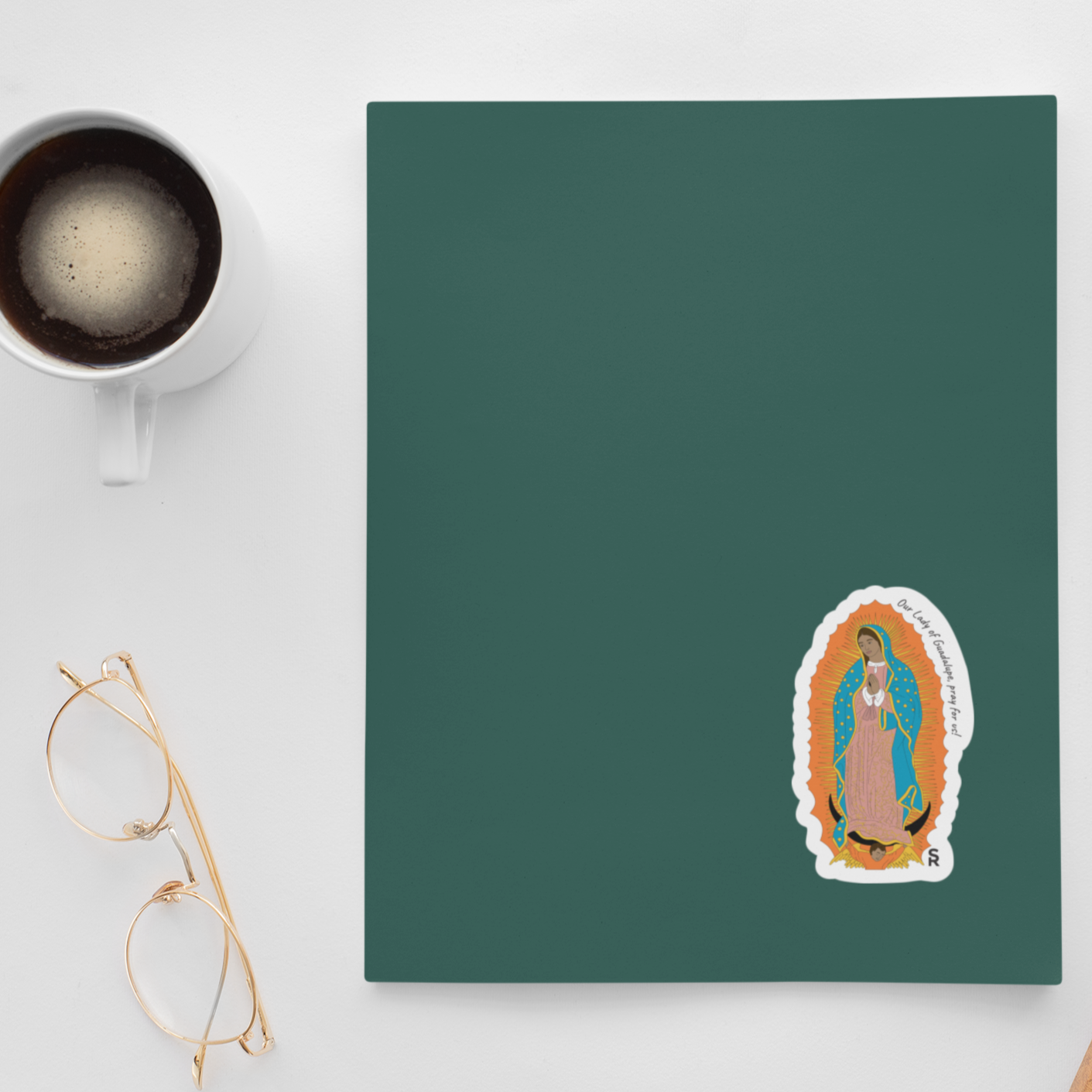 Our Lady of Guadalupe sticker that says "Our Lady of Guadalupe, pray for us" along the edge on a green notebook