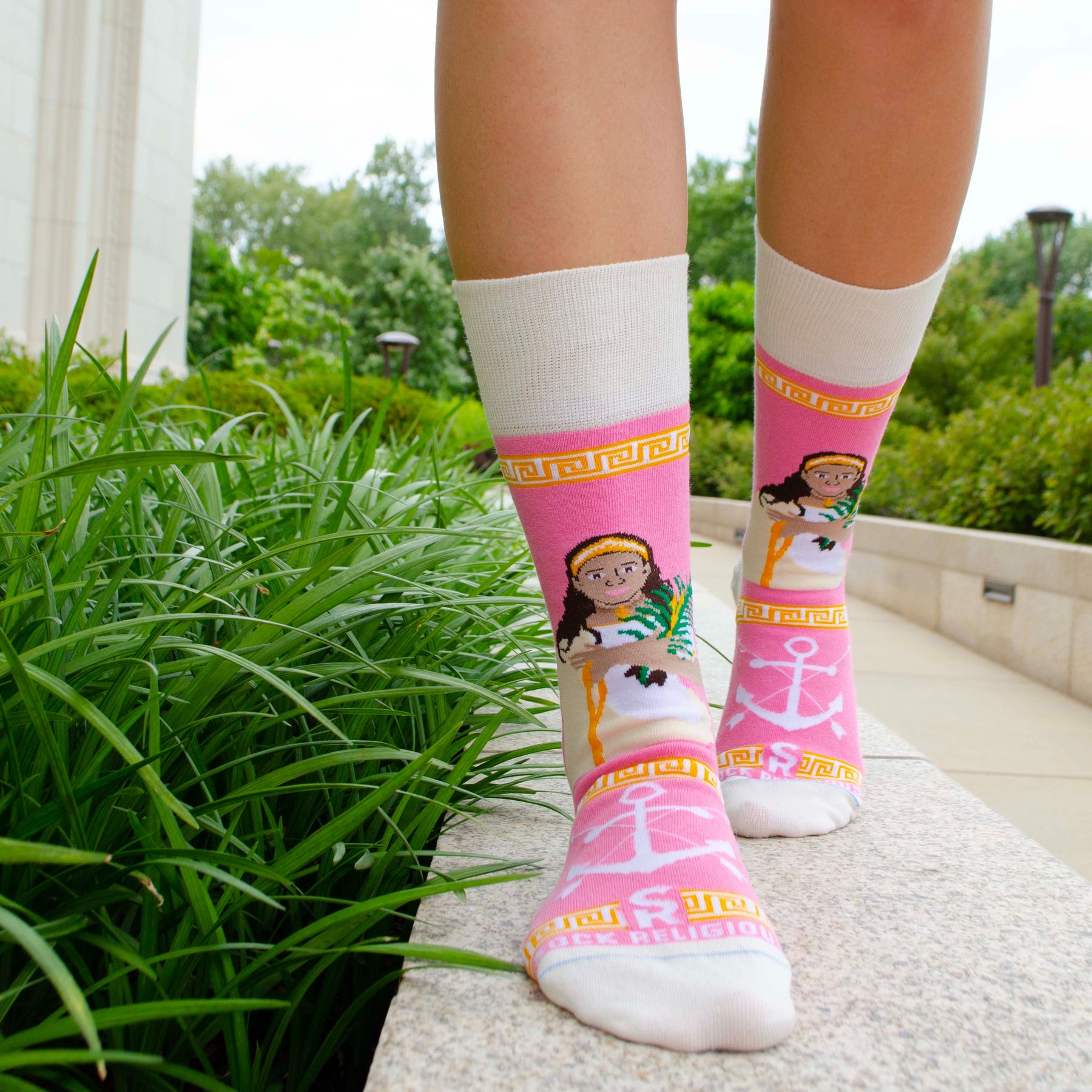 A person standing wearing a pair of pink and white socks with a picture of St. Philomena on it