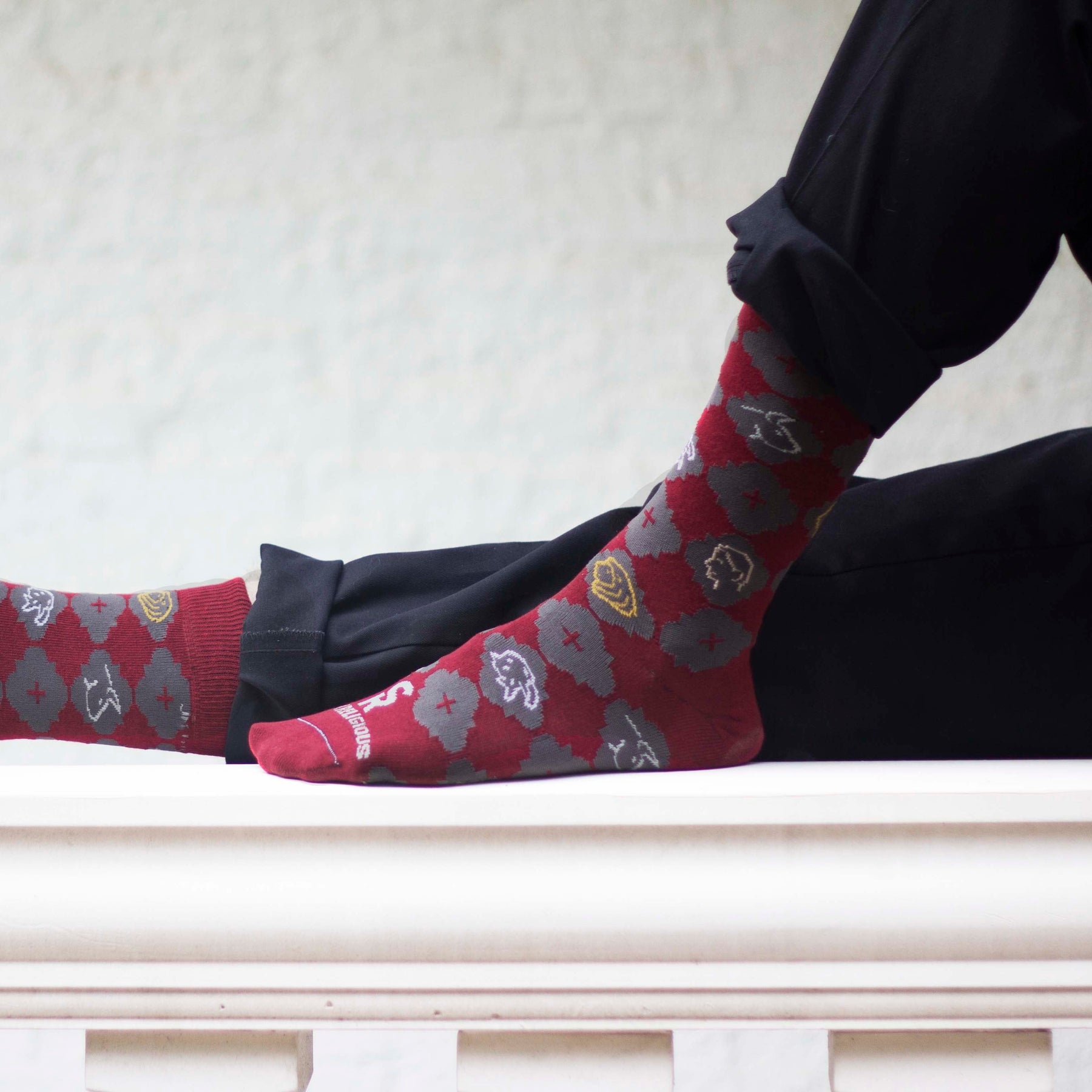 A persons sitting on the ground wearing a pair of red socks with a pattern design on it