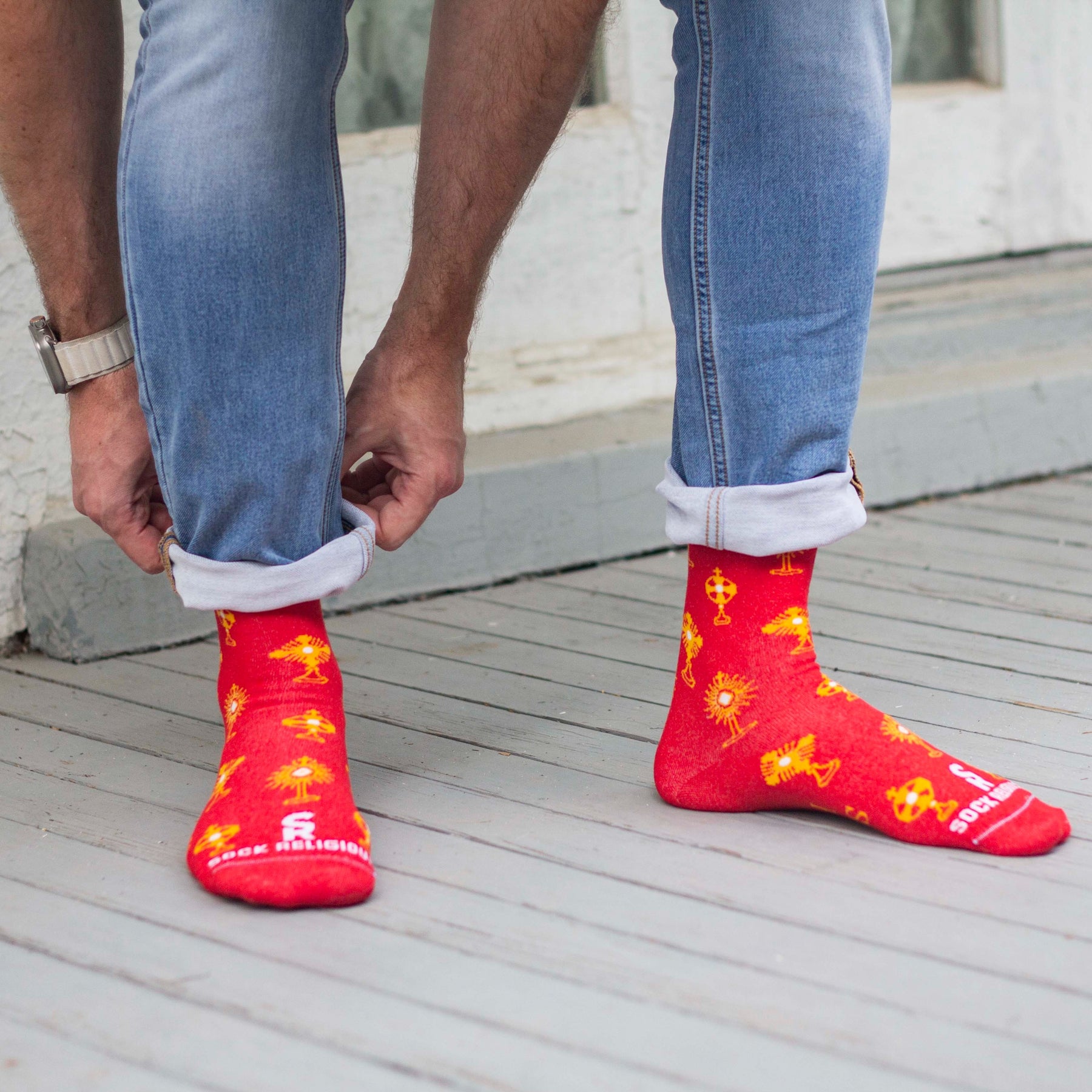 A person's foot in sleek red socks with shiny yellow designs kneeling down to adjust their pant leg