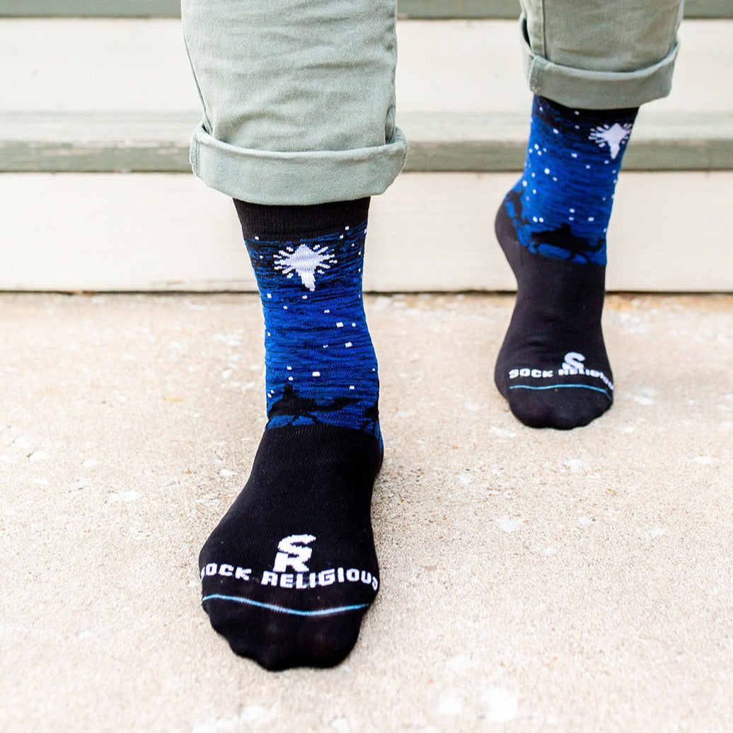 man standing wearing Black and blue socks featuring silhouettes of the 3 wisemen on camels following a bright white star of bethlehem