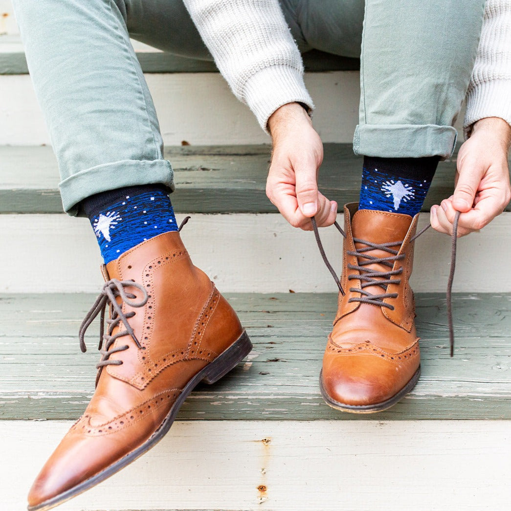 man wearing brown dress shoes with Black and blue socks featuring silhouettes of the 3 wisemen on camels following a bright white star of bethlehem