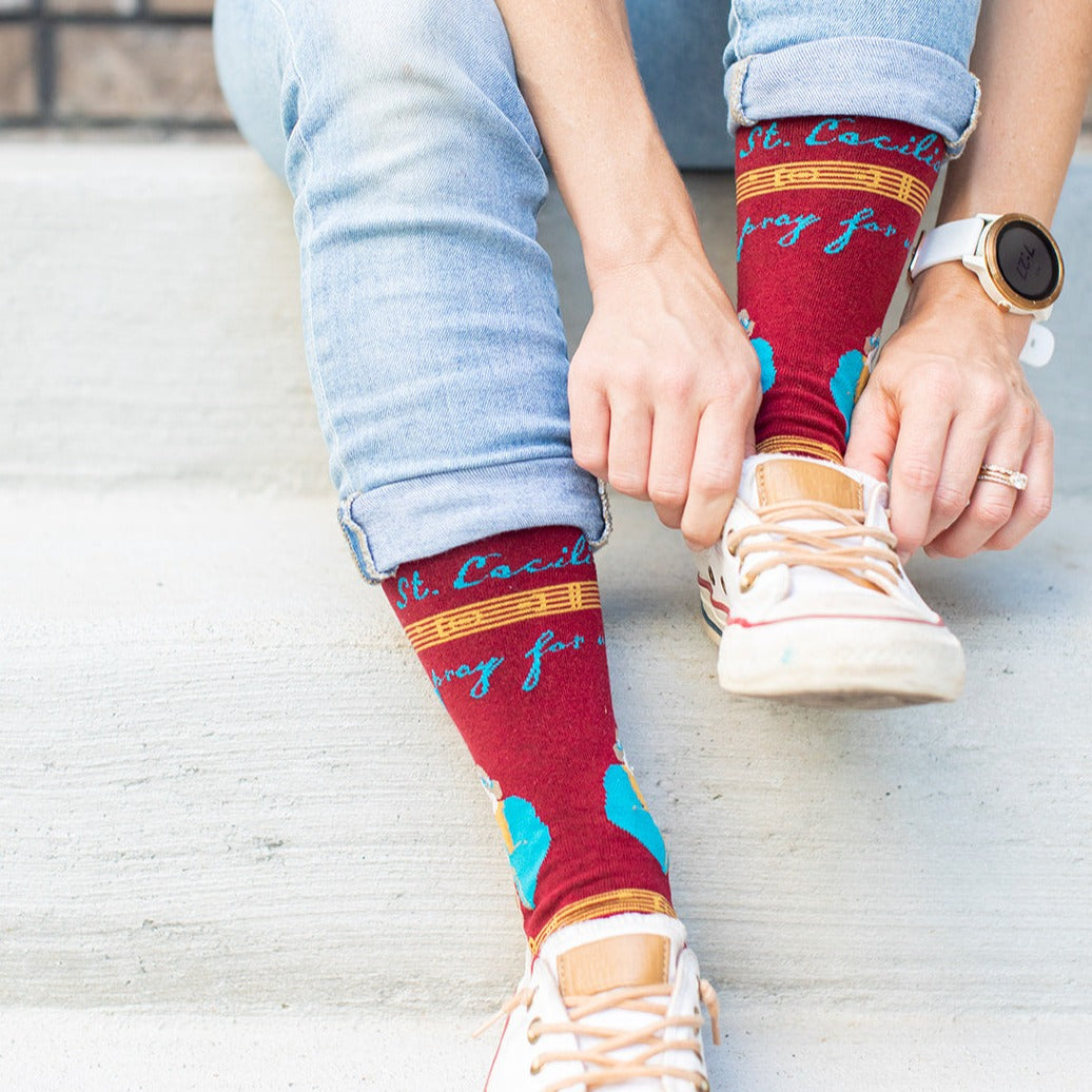 a person sitting on a step tying their shoes wearing a pair of socks with a picture of St. Cecilia