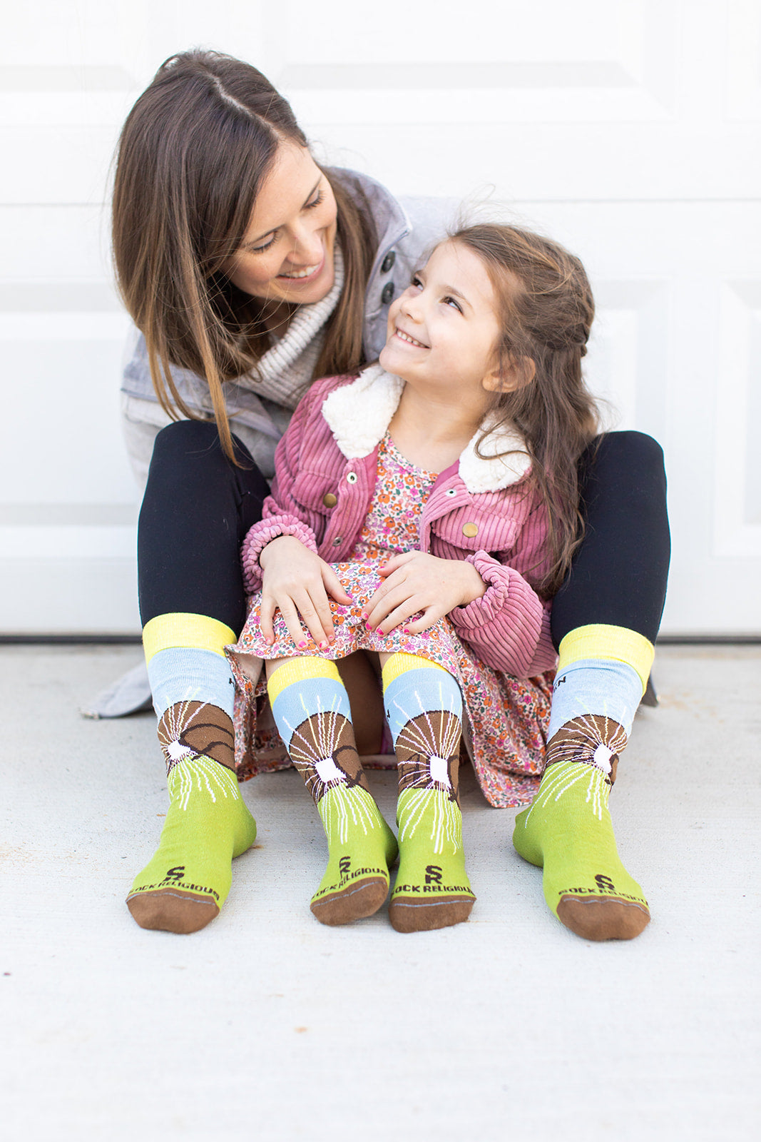 a woman and a little girl sitting on the ground wearing a pair of socks with a picture of a mountain
