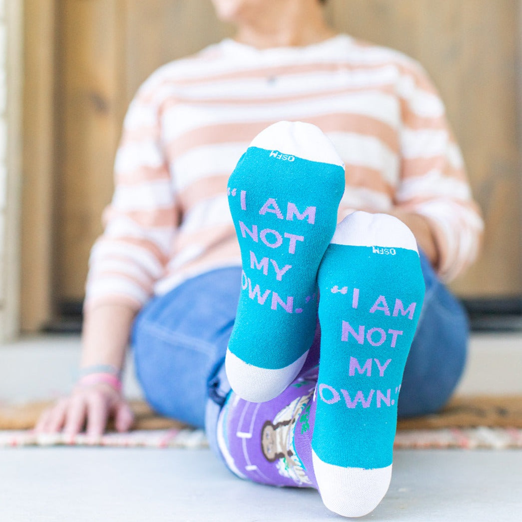 a woman sitting on the floor with her feet up wearing socks that say i am not my own