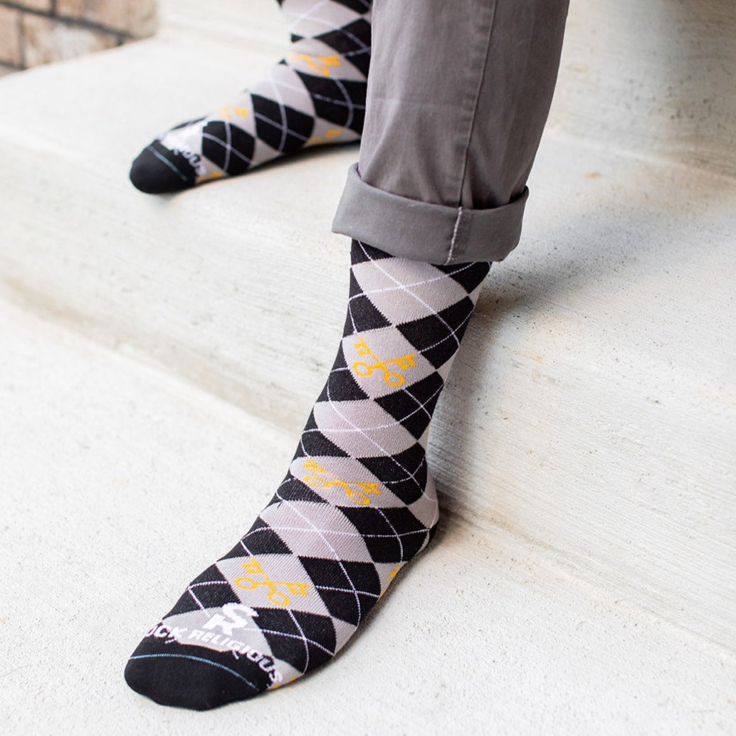 man sitting on step wearing keys to the kingdom adult socks, argyle pattern in gray and black with yellow keys