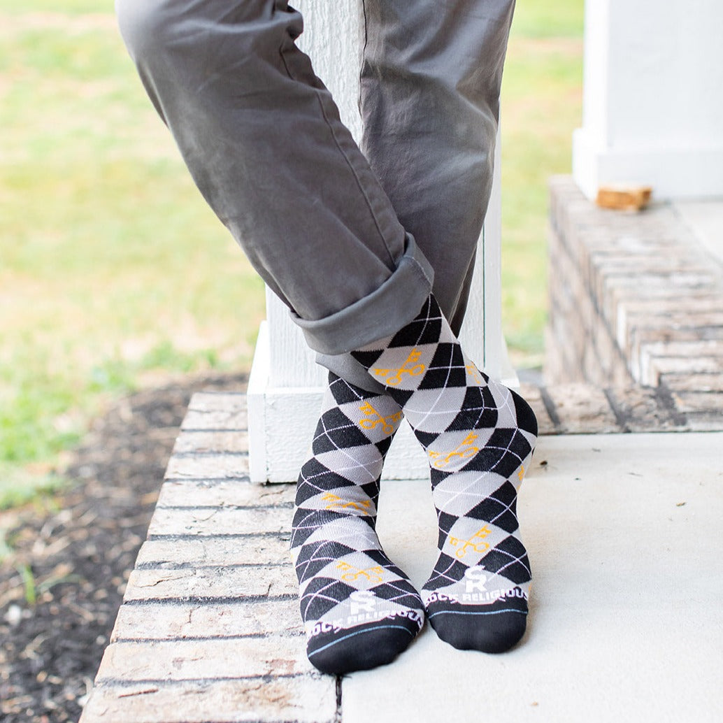 man on step wearing keys to the kingdom adult socks, argyle pattern in gray and black with yellow keys