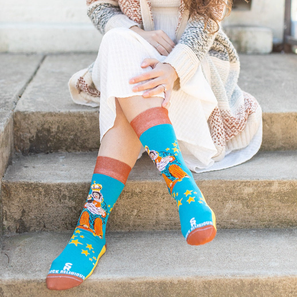 a woman sitting on the steps with her legs crossed wearing a sock with a picture of Our Lady of La Leche