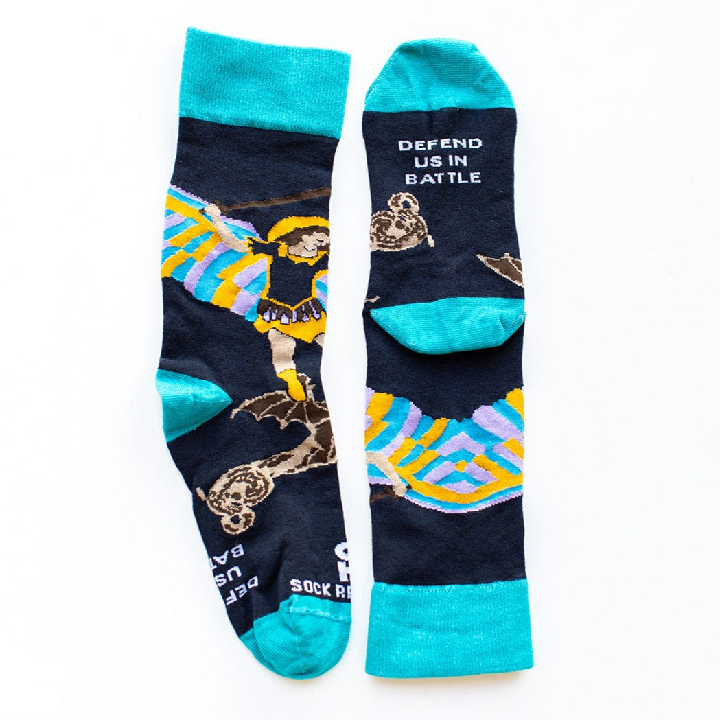 a navy pair of socks with St. Michael the Archangel slaying a demon words "defend us in battle" on bottom of foot