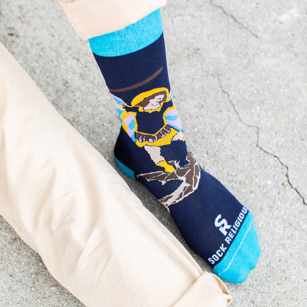 man sitting wearing navy blue socks with St. Michael the Archangel slaying a demon and the words 'defend us in battle' on the bottom of the foot