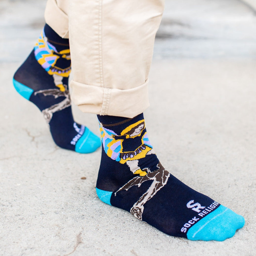 man standing on cement wearing navy blue socks with St. Michael the Archangel slaying a demon and the words 'defend us in battle' on the bottom of the foot