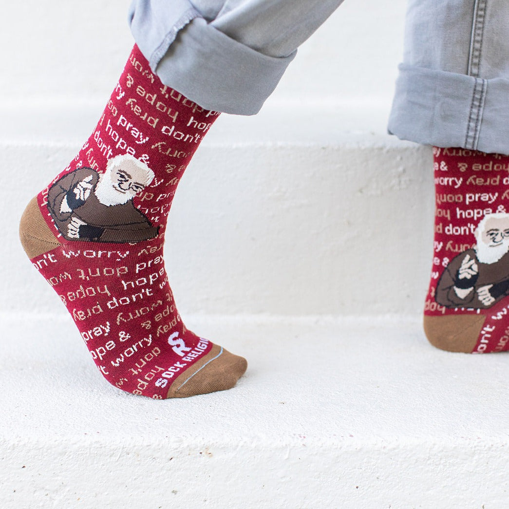 man walking wearing maroon and light brown socks that repeat 'pray, hope, and don't worry' in the background and feature St. Padre Pio