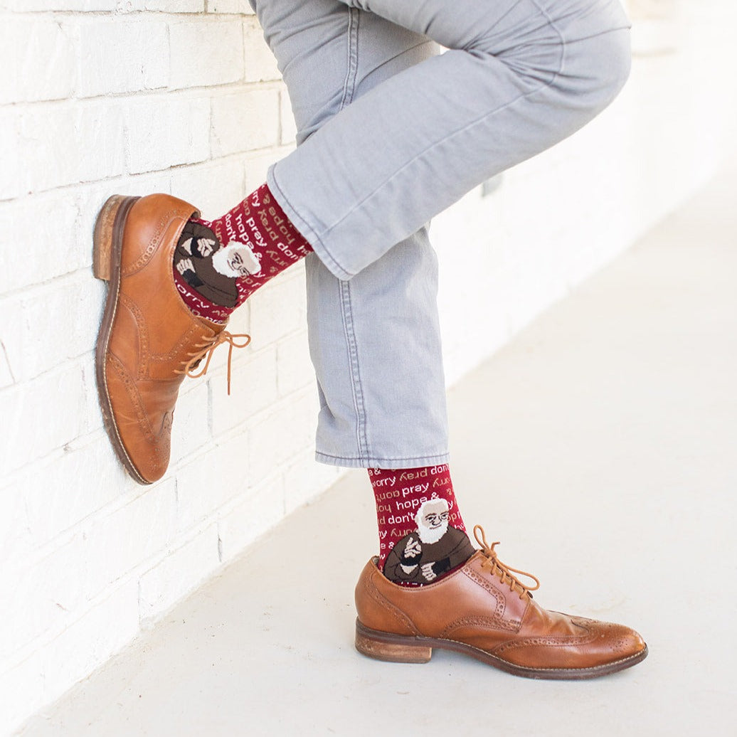 man wearing brown dress shoes and maroon and light brown socks that repeat 'pray, hope, and don't worry' in the background and feature St. Padre Pio