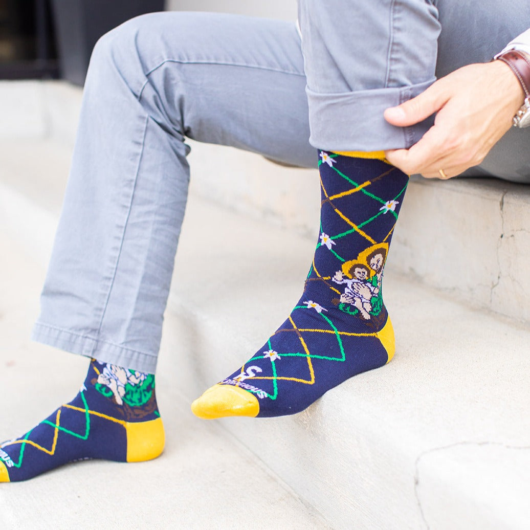 man sitting on step wearing Navy blue St. Joseph adult XL socks with Joseph holding baby Jesus. Yellow and green argyle lines