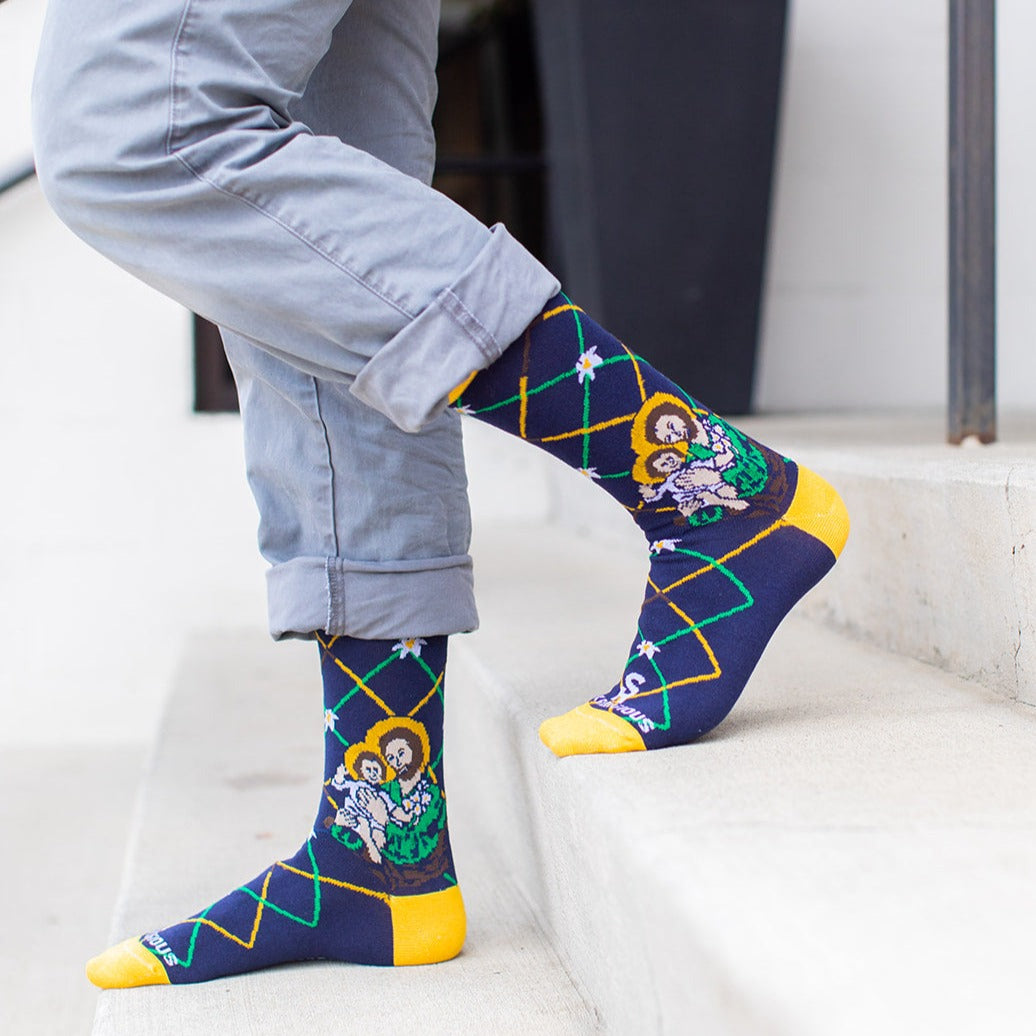 man standing on step wearing Navy blue St. Joseph adult XL socks with Joseph holding baby Jesus. Yellow and green argyle lines