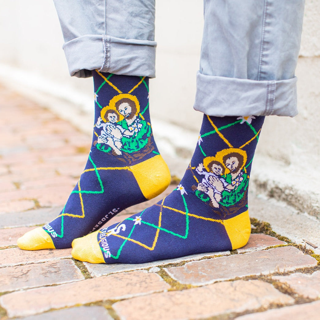 man standing on brick wearing Navy blue St. Joseph adult XL socks with Joseph holding baby Jesus. Yellow and green argyle lines