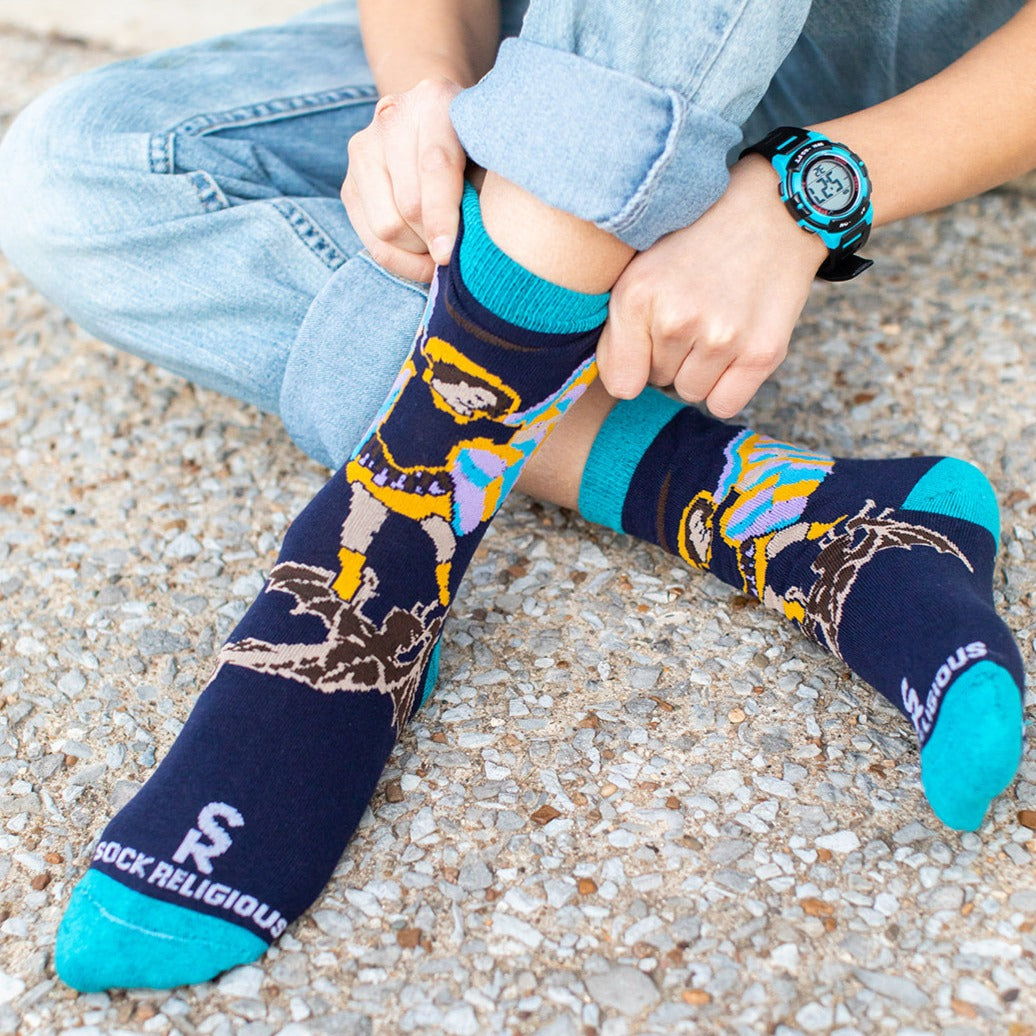 boy wearing navy blue socks with St. Michael the Archangel slaying a demon and the words 'defend us in battle' on the bottom of the foot