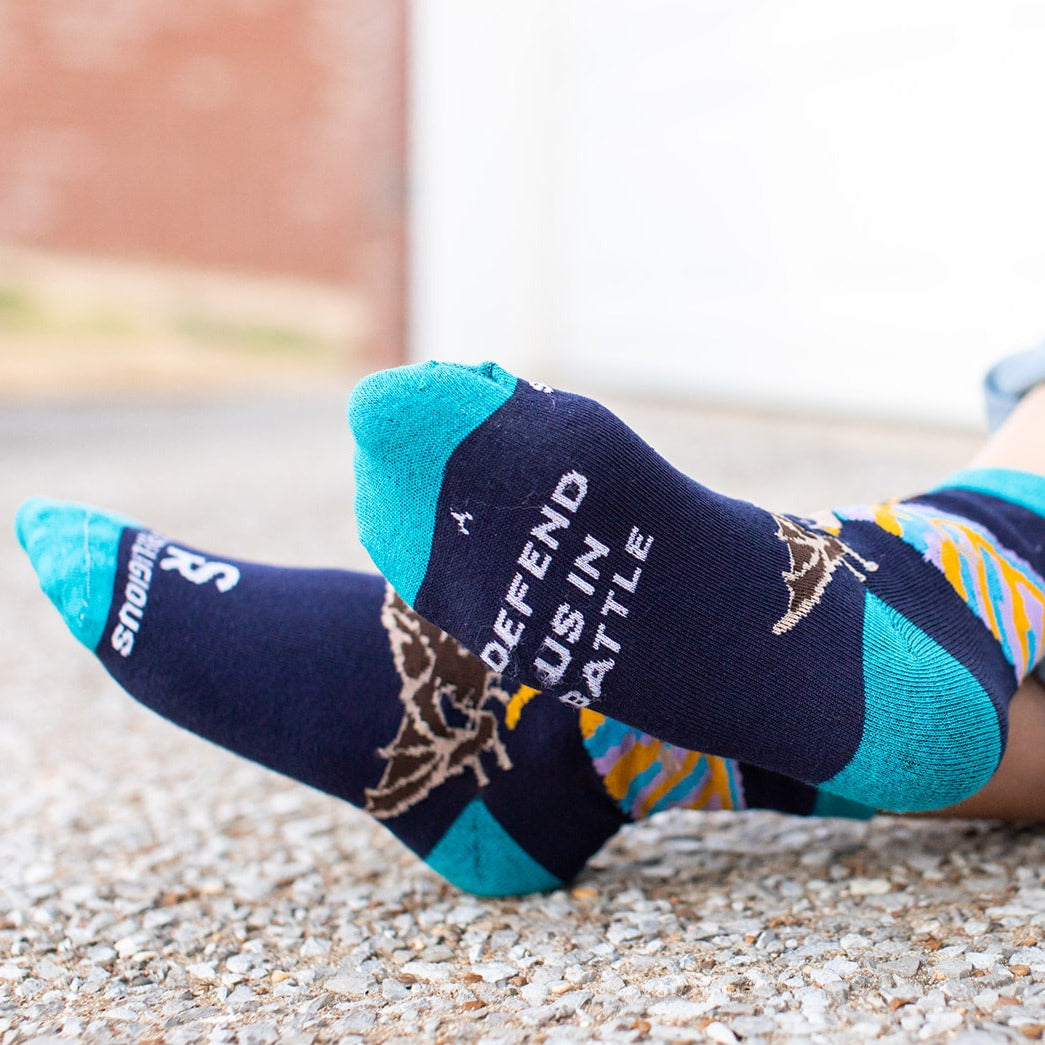 boy showing bottom of foot of navy blue socks with St. Michael the Archangel slaying a demon and the words 'defend us in battle' on the bottom of the foot