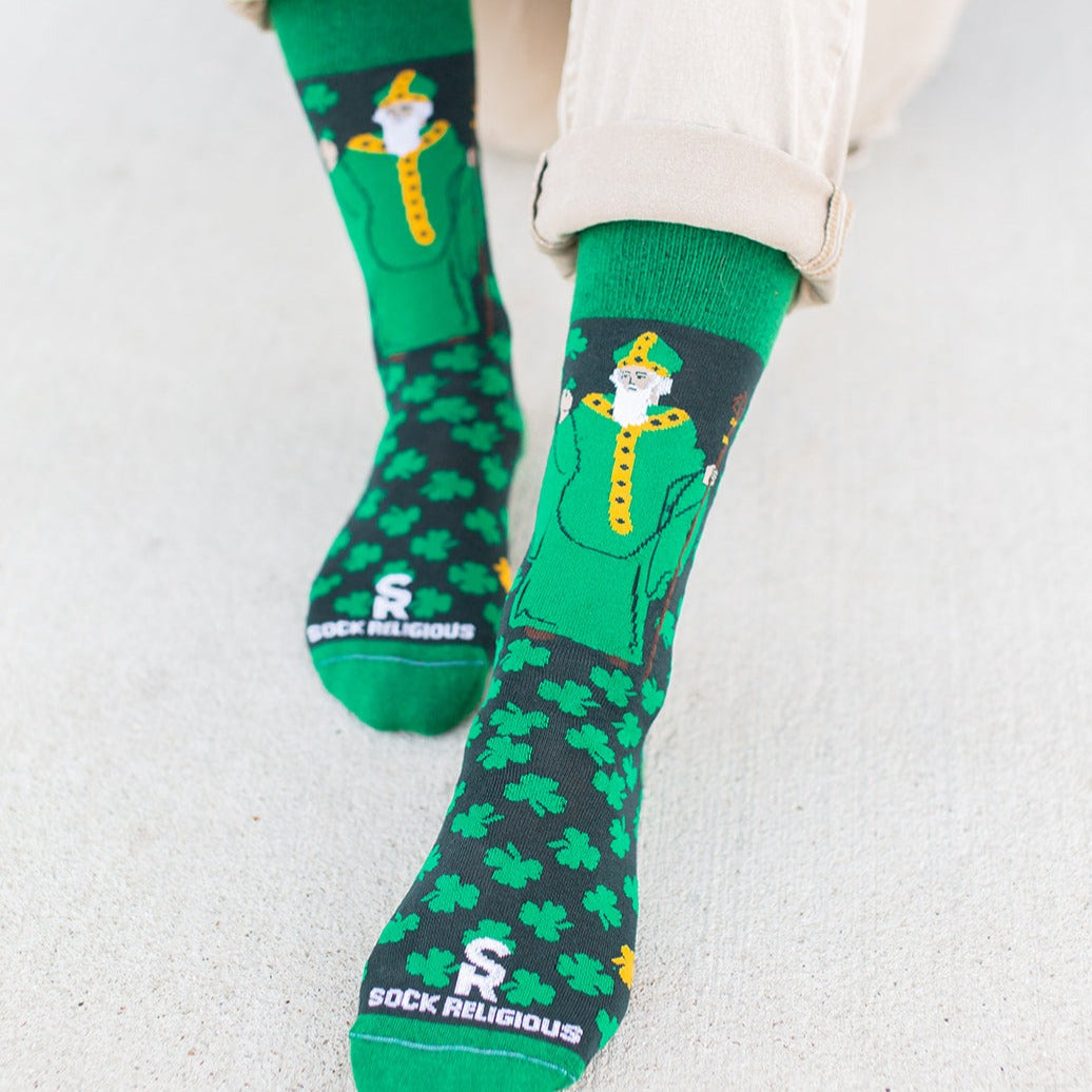 man sitting on cement wearing Green socks with green clovers and St. Patrick of Ireland