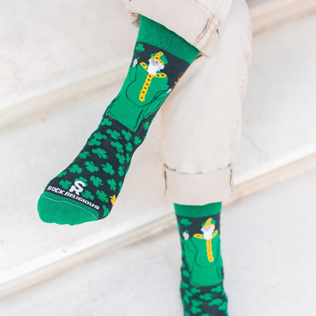man sitting on steps with legs crossed wearing Green socks with green clovers and St. Patrick of Ireland