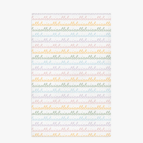 White colored, waffle textured dish towel laid flat with the design that says alleluia, alleluia repeatedly in cursive writing, in colors pastel pink, pastel yellow, pastel blue and pastel green.