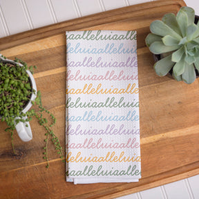 White colored, waffle textured dish towel folded in half with the design that says alleluia, alleluia repeatedly in cursive writing, in colors pastel pink, pastel yellow, pastel blue and pastel green.