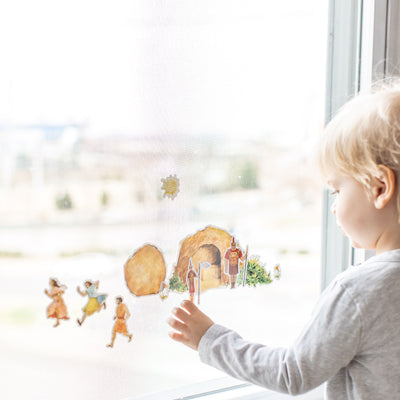 little boy playing with empty tomb cling set on a window