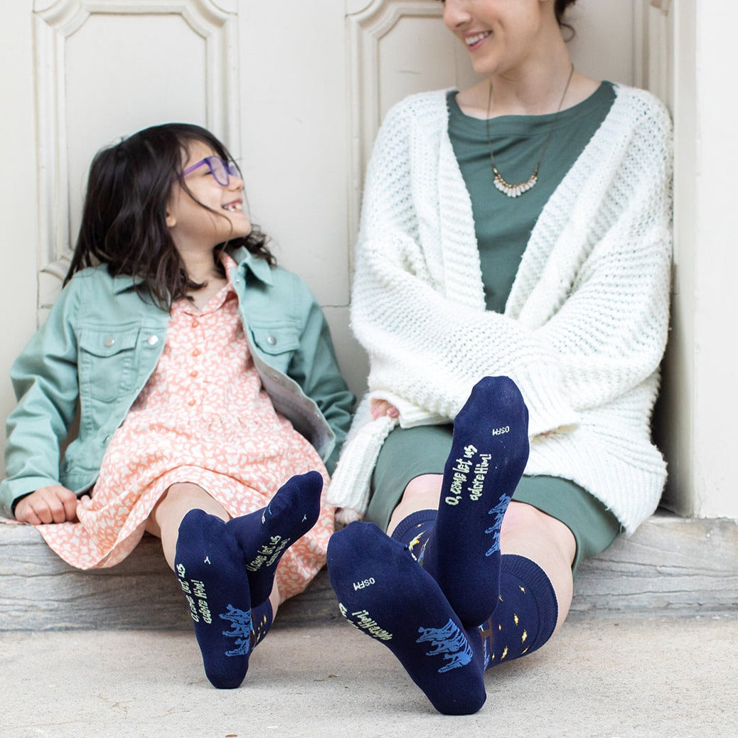 mother and child wearing matching nativity socks showing bottom of feet and "o come let us adore him" words on the bottom