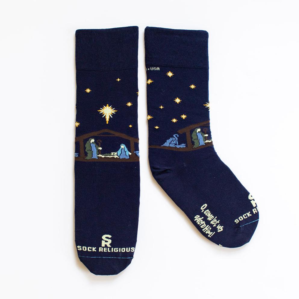 a pair of navy dress socks with a nativity scene on them  "o come let us adore him" is on the bottom