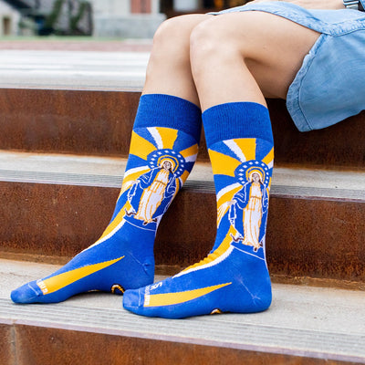 woman sitting on steps wearing Our Lady of Grace socks with Mary, yellow and blue rays and a serpant on the bottom of the foot