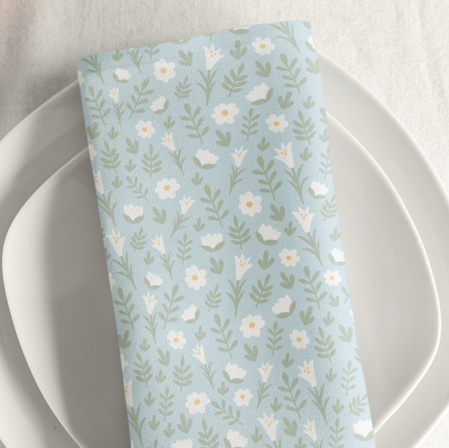 Light blue Easter Alleluia napkin with white floral design placed on a plate in a styled table setting.