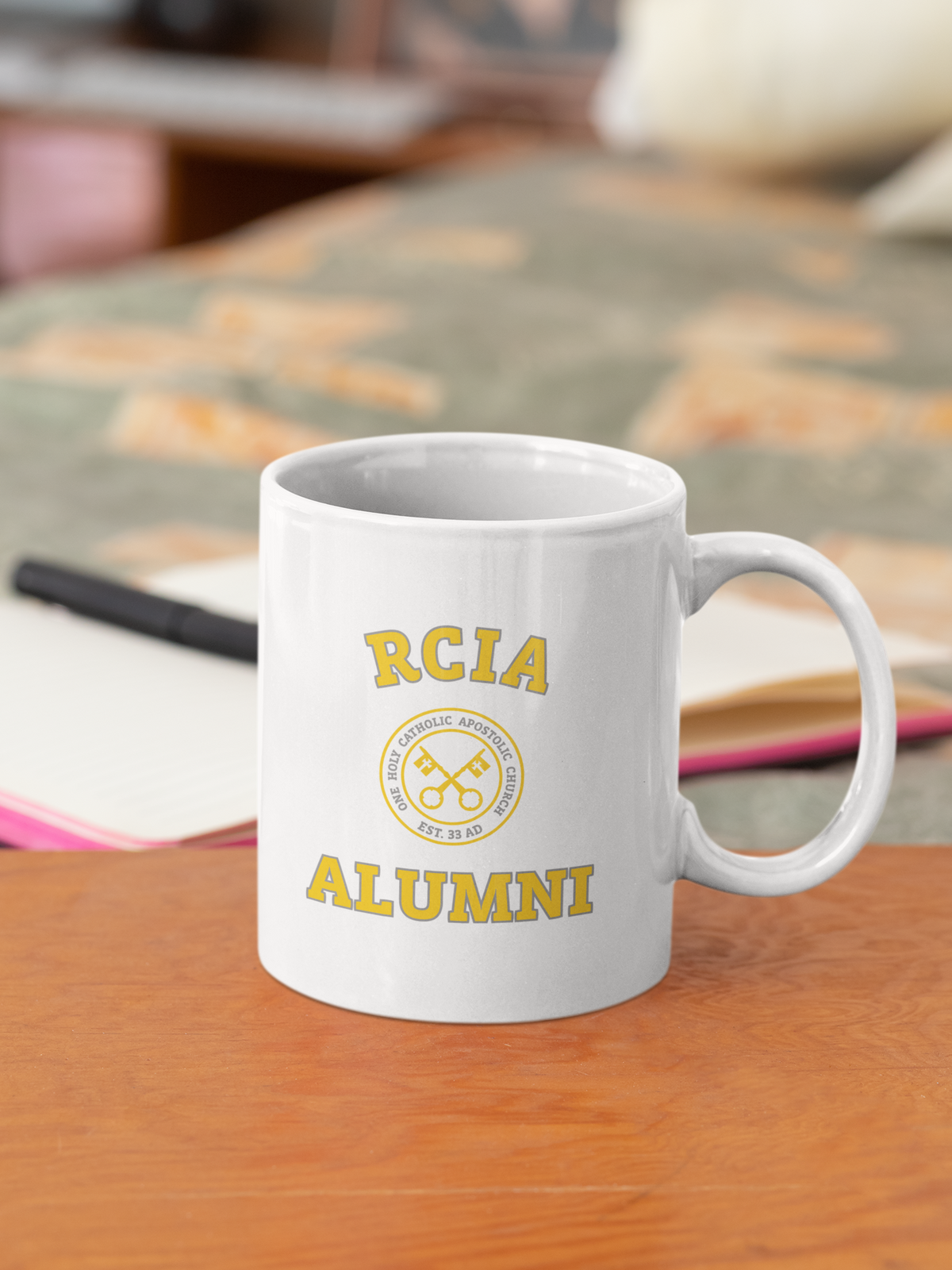 front of mug that says "RICA Alumni" in yellow with keys in the middle surrounded by words 'one, holy, catholic, apostolic' and 'est. 33 AD'