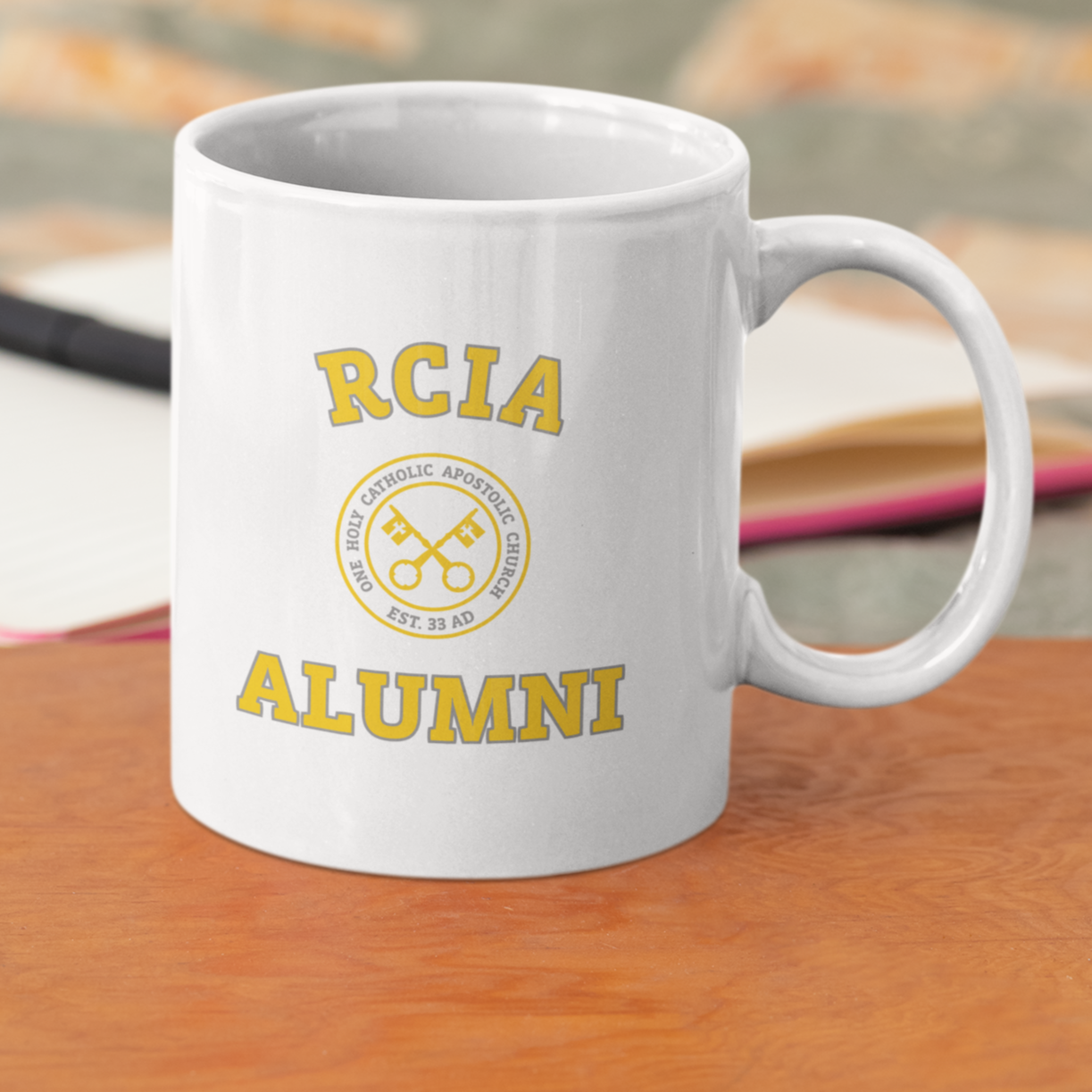 front of mug that says "RICA Alumni" in yellow with keys in the middle surrounded by words 'one, holy, catholic, apostolic' and 'est. 33 AD'